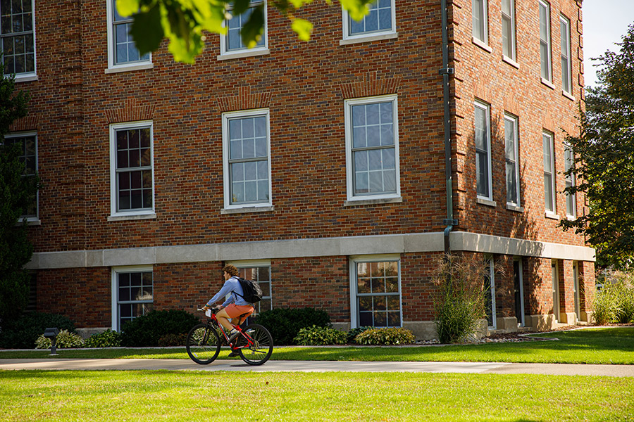 An Albion College student cycles past Robinson Hall on the campus Quad.