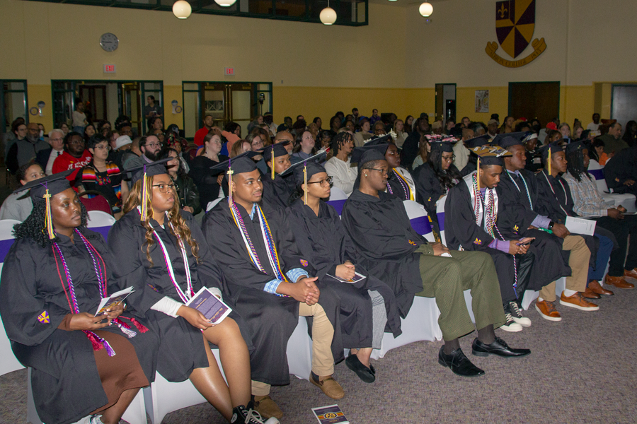 Students wearing academic regalia watch as remarks are given at a commencement ceremony.